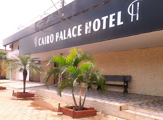Fachada do Cairo Palace Hotel vista da calçada da Avenida Bernardo Sayão, com o letreiro escuro, palmeiras em floreiras de tijolo e o pátio de estacionamento.